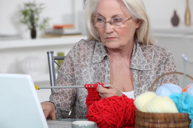 Mature woman knitting at computer looking unhappy